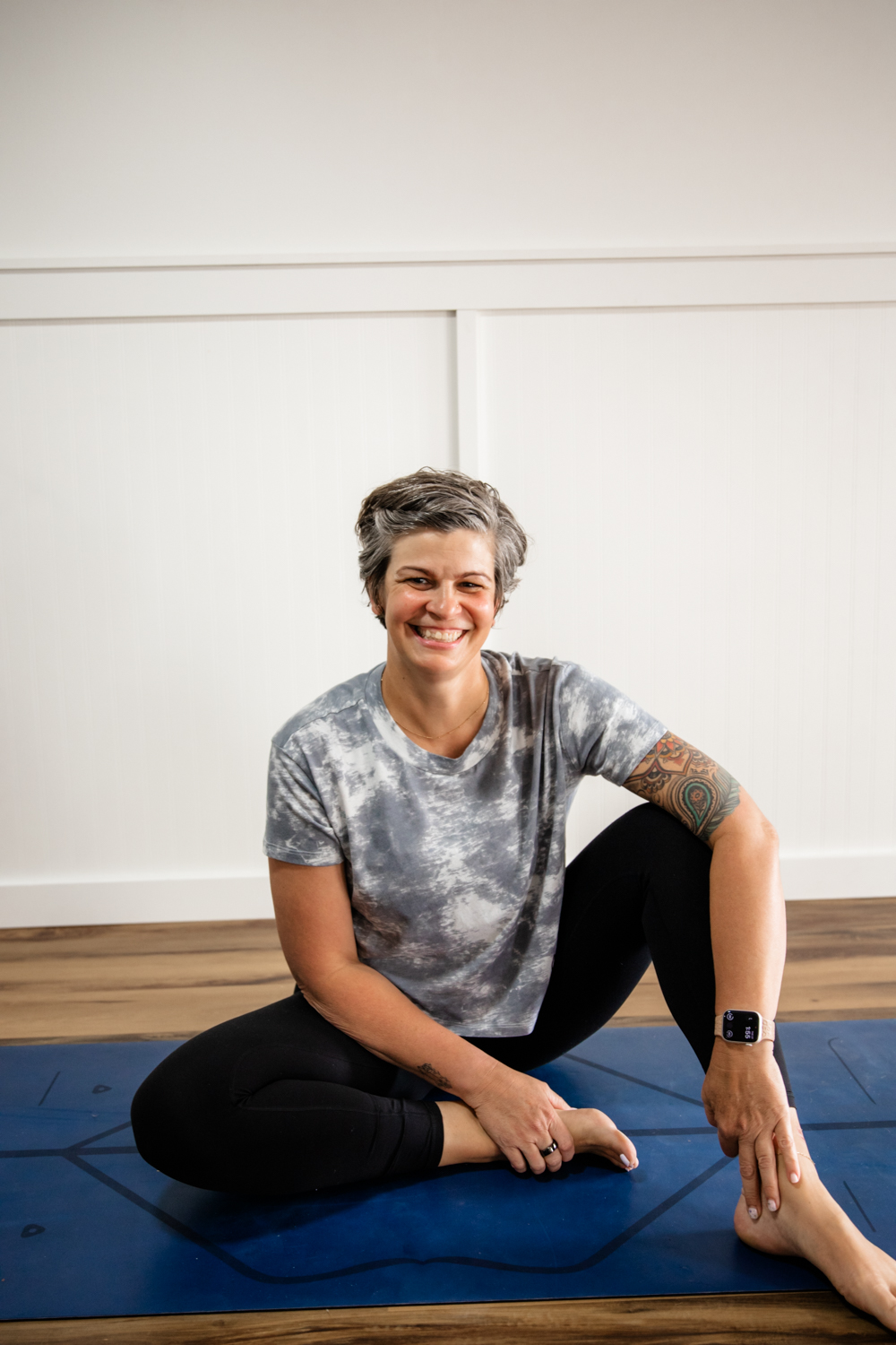 Yoga teacher sitting on a couch with shelf of wellness products behind her.